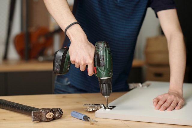 hands of youthful boy holding electric drill while fixing hinge on door